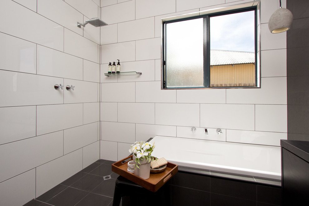 Design ideas for a medium sized contemporary ensuite bathroom in Dunedin with a vessel sink, flat-panel cabinets, black cabinets, laminate worktops, a built-in bath, a walk-in shower, grey tiles, porcelain tiles, grey walls and porcelain flooring.