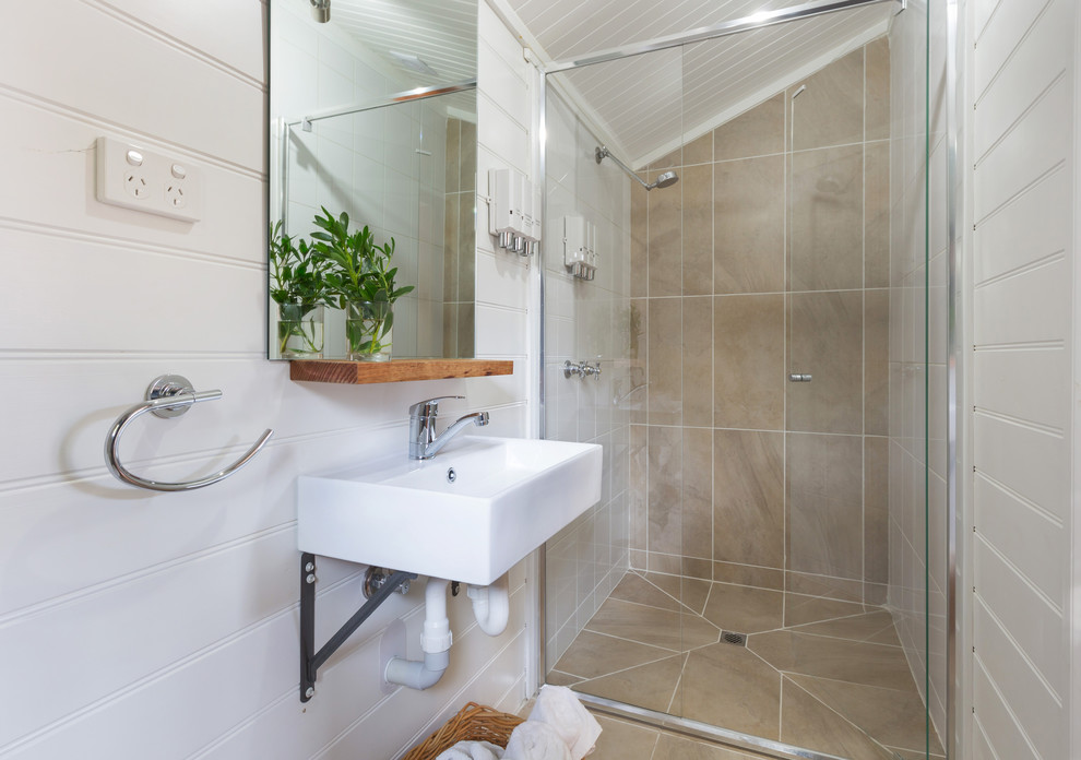 Foto på ett litet maritimt badrum med dusch, med en dusch i en alkov, beige kakel, vita väggar, ett väggmonterat handfat och dusch med gångjärnsdörr
