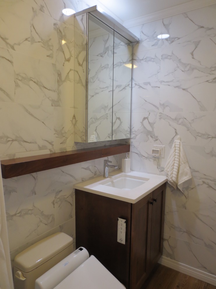 Klassisk inredning av ett litet badrum med dusch, med luckor med infälld panel, skåp i mellenmörkt trä, ett platsbyggt badkar, en dusch i en alkov, en toalettstol med hel cisternkåpa, vit kakel, porslinskakel, vita väggar, vinylgolv, ett undermonterad handfat och bänkskiva i akrylsten