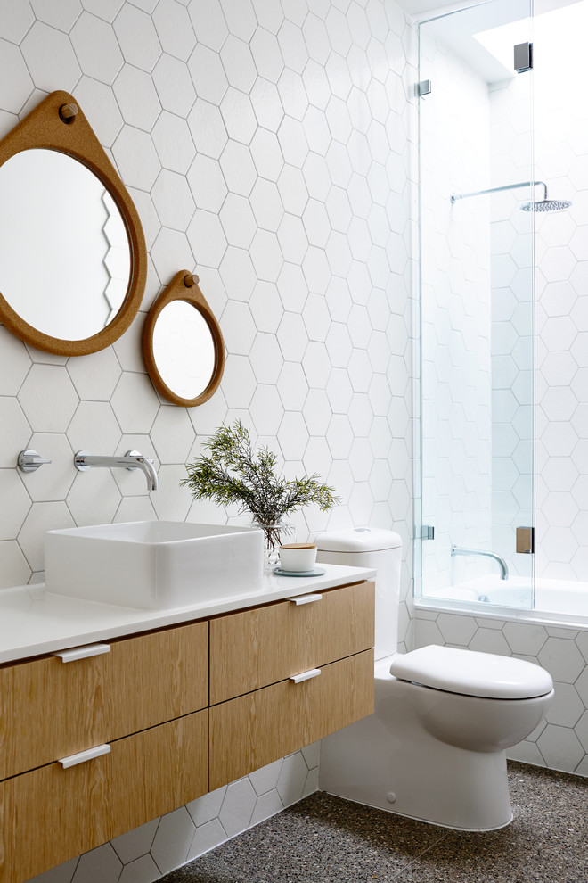 Пример оригинального дизайна: ванная комната в современном стиле с настольной раковиной, плоскими фасадами, светлыми деревянными фасадами, ванной в нише, душем над ванной, раздельным унитазом, белой плиткой и душевой кабиной
