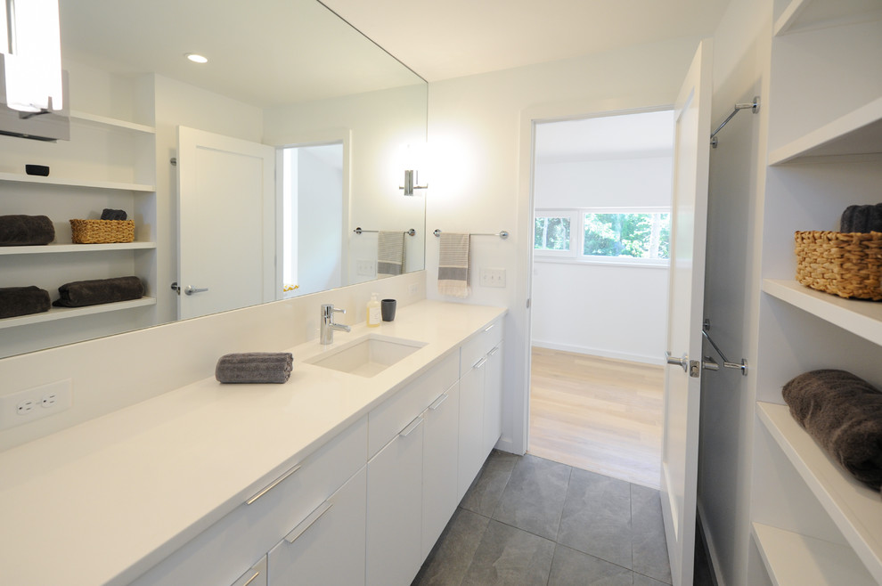 Идея дизайна: ванная комната среднего размера в стиле модернизм с плоскими фасадами, белыми фасадами, душем в нише, унитазом-моноблоком, белой плиткой, керамогранитной плиткой, белыми стенами, полом из керамогранита, врезной раковиной, столешницей из искусственного кварца, серым полом и душем с распашными дверями
