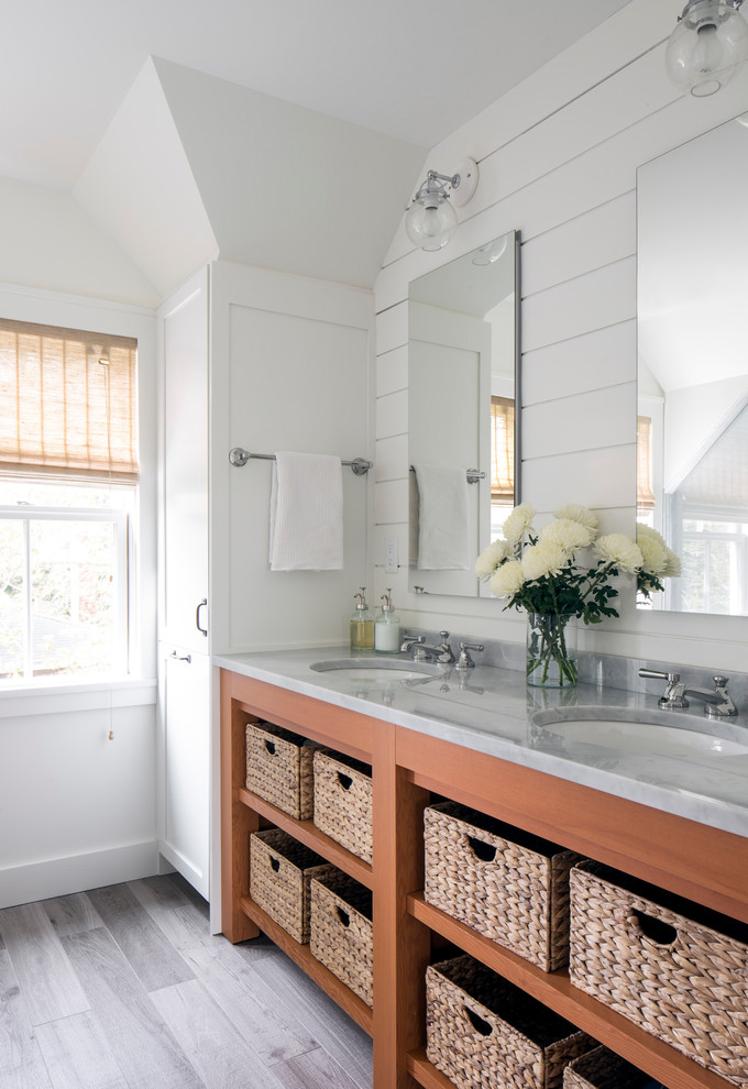 Cette image montre une salle de bain principale marine en bois brun de taille moyenne avec un mur blanc, un plan de toilette en marbre, un plan de toilette gris, un placard sans porte, un lavabo encastré et un sol gris.