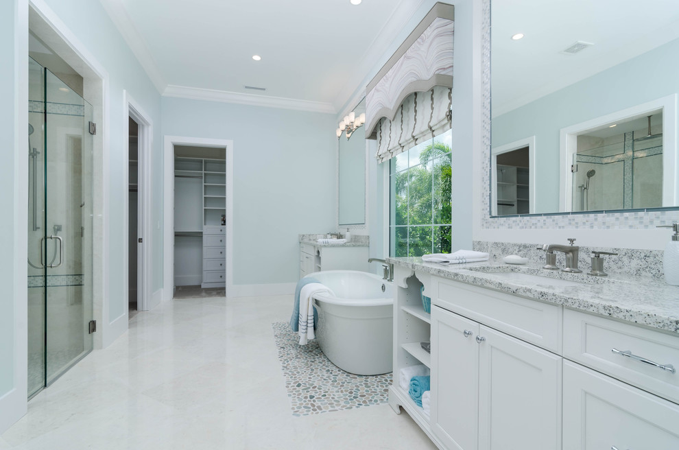 Photo of a large classic ensuite bathroom in Miami with white cabinets, a freestanding bath, a corner shower, a two-piece toilet, blue tiles, mosaic tiles, blue walls, limestone flooring, a built-in sink, granite worktops, beige floors and a hinged door.