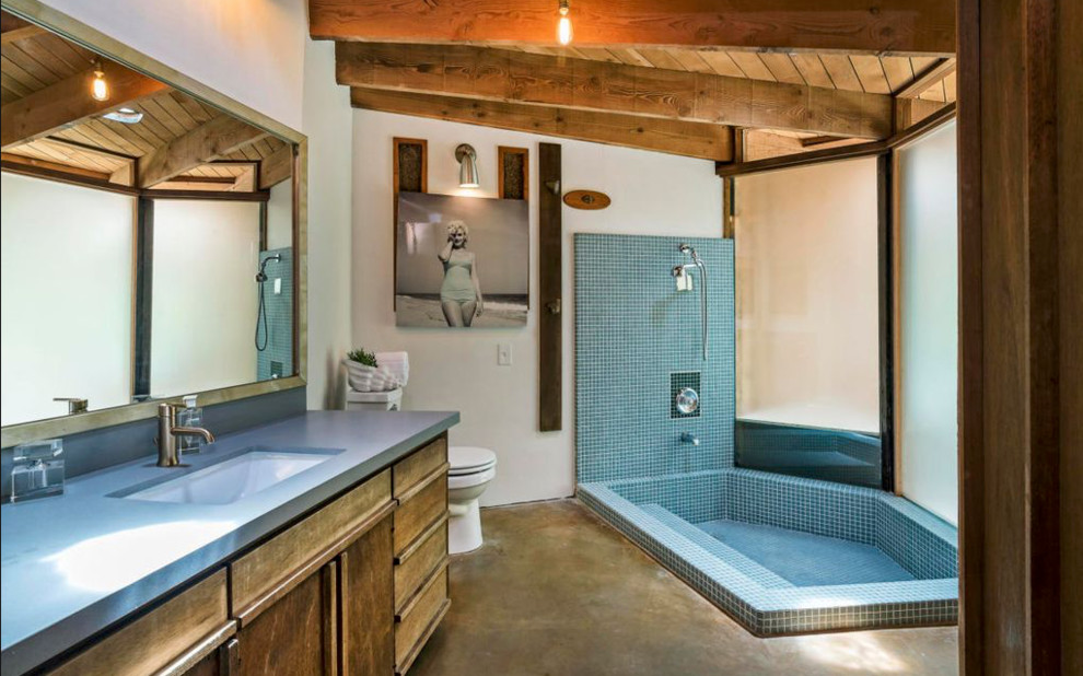 60 tals inredning av ett grå grått en-suite badrum, med släta luckor, skåp i mellenmörkt trä, en dusch/badkar-kombination, blå kakel, vita väggar, betonggolv, ett undermonterad handfat, brunt golv, med dusch som är öppen och mosaik