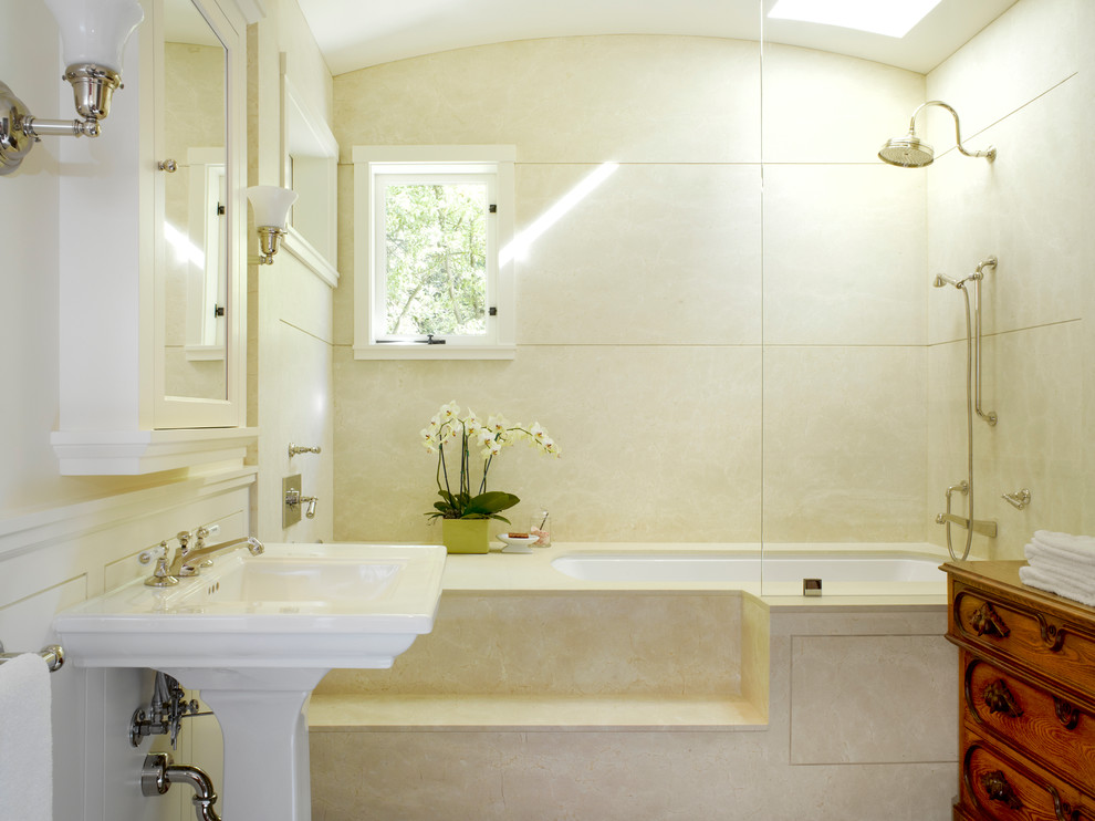 Стильный дизайн: главная ванная комната среднего размера в классическом стиле с раковиной с пьедесталом, темными деревянными фасадами, полновстраиваемой ванной, душем над ванной, каменной плиткой, белыми стенами и бежевой плиткой - последний тренд