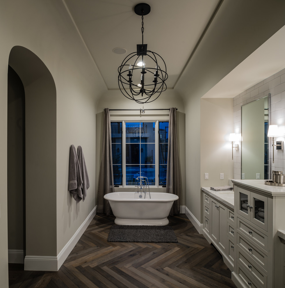 На фото: главная ванная комната в стиле неоклассика (современная классика) с фасадами с утопленной филенкой, белыми фасадами, отдельно стоящей ванной, бежевыми стенами, темным паркетным полом и врезной раковиной
