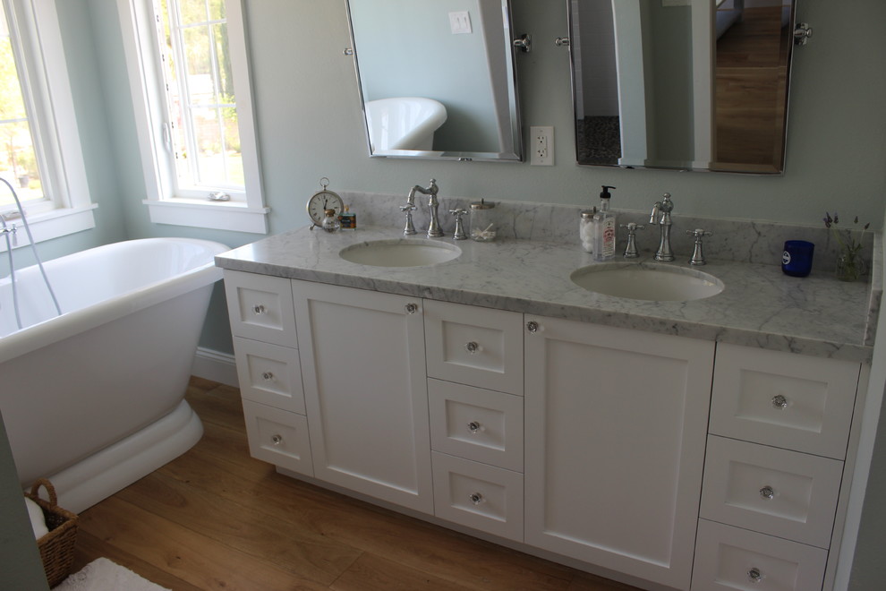 Elegant laminate floor freestanding bathtub photo in Los Angeles with an undermount sink, shaker cabinets, white cabinets, marble countertops and green walls