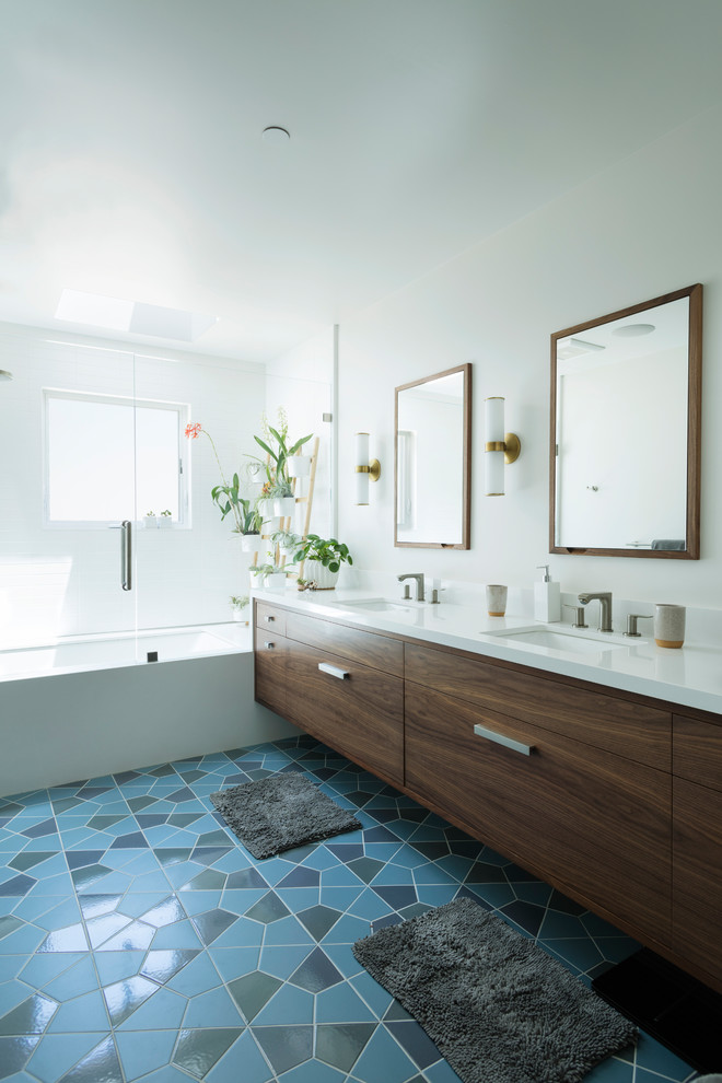 На фото: главная ванная комната среднего размера в стиле модернизм с плоскими фасадами, фасадами цвета дерева среднего тона, угловой ванной, душем над ванной, унитазом-моноблоком, белой плиткой, плиткой мозаикой, белыми стенами, полом из керамической плитки, врезной раковиной, столешницей из искусственного кварца, синим полом, душем с распашными дверями, белой столешницей, сиденьем для душа, тумбой под две раковины и подвесной тумбой