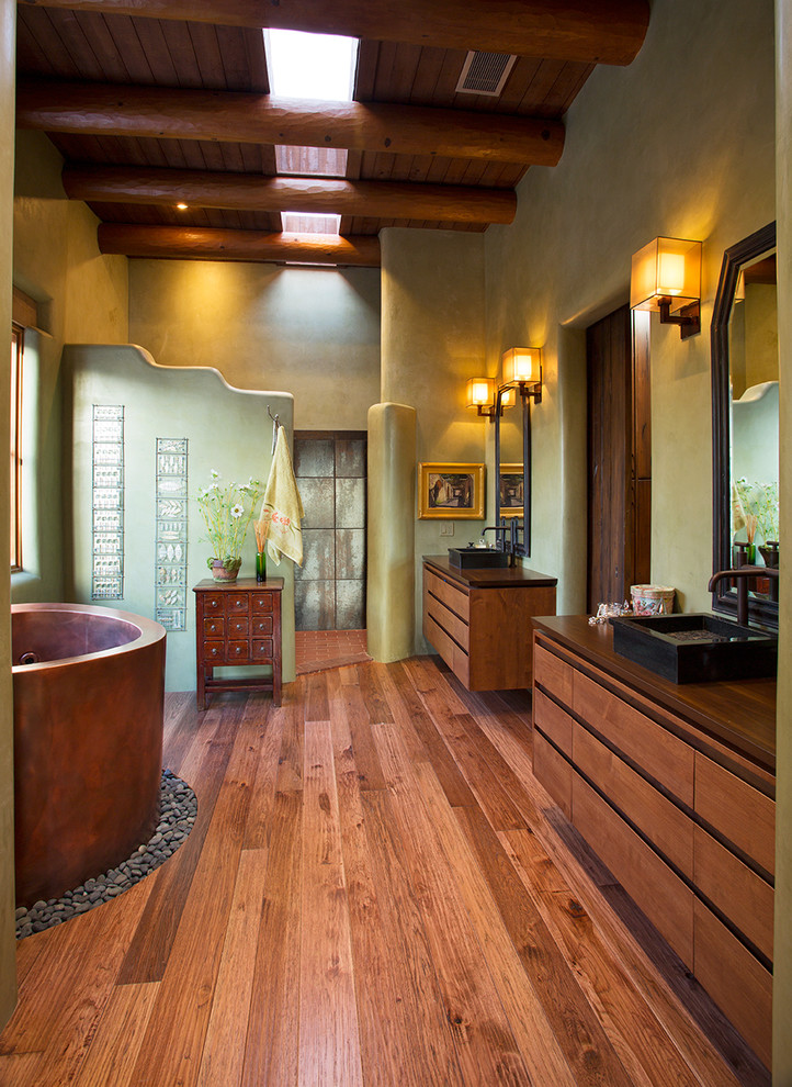 Cette image montre une salle de bain principale sud-ouest américain en bois brun avec une vasque, un placard à porte plane, un bain japonais, une douche ouverte, un mur beige, un sol en bois brun et aucune cabine.