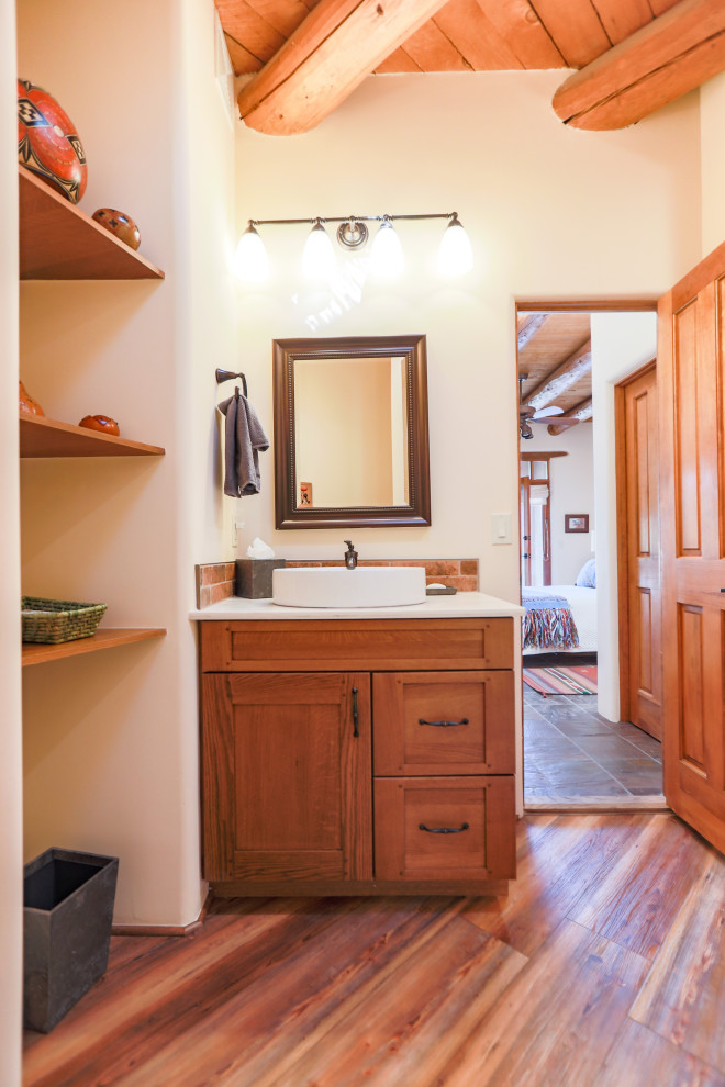 Пример оригинального дизайна: маленькая ванная комната в стиле неоклассика (современная классика) с фасадами в стиле шейкер, фасадами цвета дерева среднего тона, ванной в нише, душем над ванной, унитазом-моноблоком, бежевой плиткой, полом из плитки под дерево, душевой кабиной, раковиной с пьедесталом, разноцветным полом, душем с раздвижными дверями, белой столешницей, тумбой под одну раковину, встроенной тумбой, балками на потолке и столешницей из искусственного камня для на участке и в саду