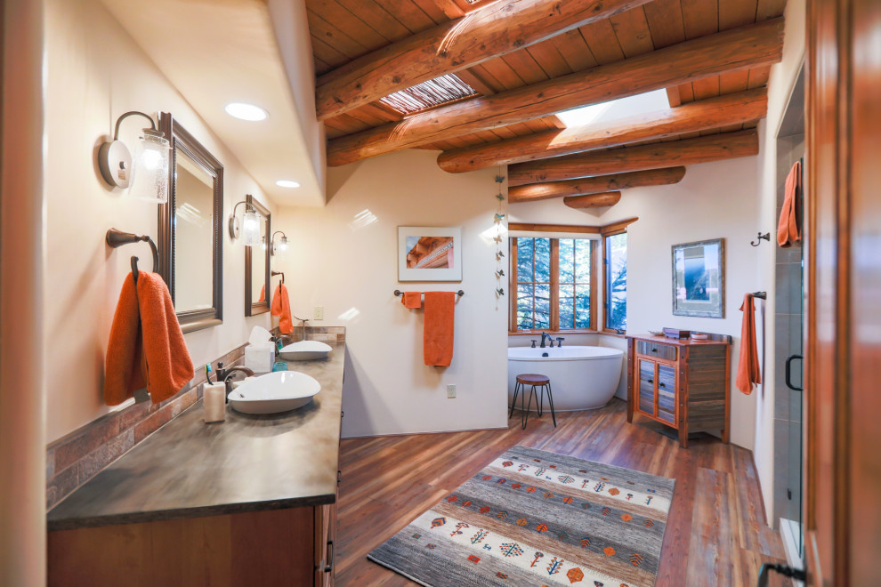 Example of a huge southwest master multicolored tile and ceramic tile wood-look tile floor, multicolored floor, double-sink and exposed beam bathroom design in Albuquerque with medium tone wood cabinets, a one-piece toilet, white walls, a pedestal sink, solid surface countertops, black countertops, a built-in vanity, a hinged shower door and raised-panel cabinets