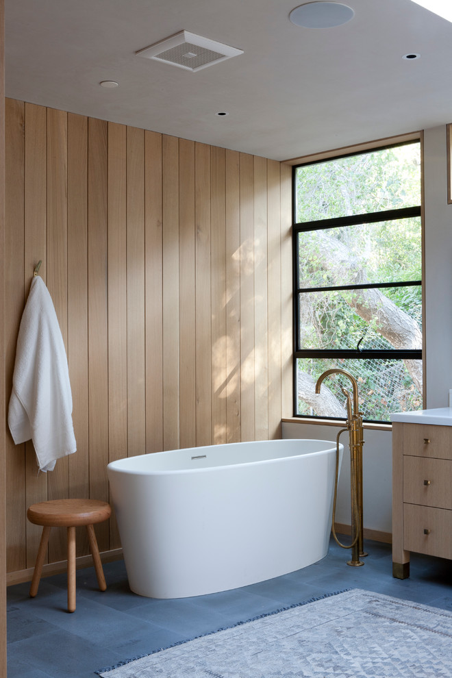 Идея дизайна: большая главная ванная комната в стиле модернизм с светлыми деревянными фасадами, отдельно стоящей ванной, каменной плиткой и мраморной столешницей