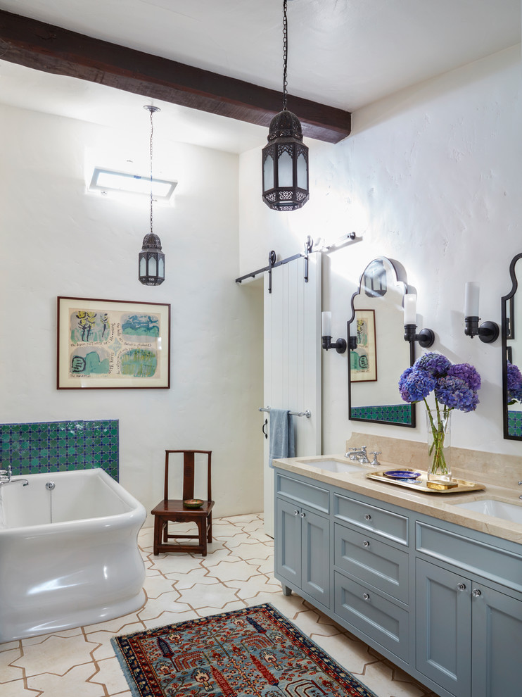 Idée de décoration pour une douche en alcôve principale méditerranéenne avec un placard avec porte à panneau encastré, des portes de placard bleues, une baignoire d'angle, un carrelage multicolore, mosaïque, un mur blanc, carreaux de ciment au sol, un lavabo encastré, un plan de toilette en calcaire, un sol blanc et un plan de toilette beige.