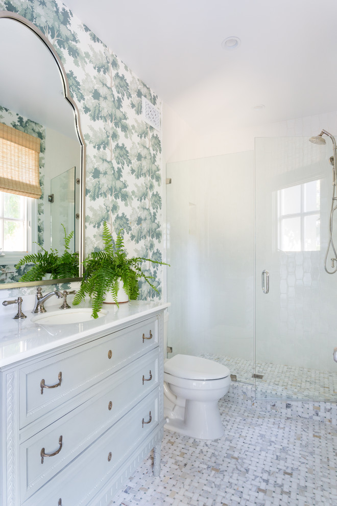 На фото: маленькая ванная комната в стиле неоклассика (современная классика) с фасадами островного типа, синими фасадами, душем в нише, унитазом-моноблоком, белой плиткой, керамогранитной плиткой, разноцветными стенами, полом из мозаичной плитки, душевой кабиной, врезной раковиной, мраморной столешницей, разноцветным полом, душем с распашными дверями и белой столешницей для на участке и в саду