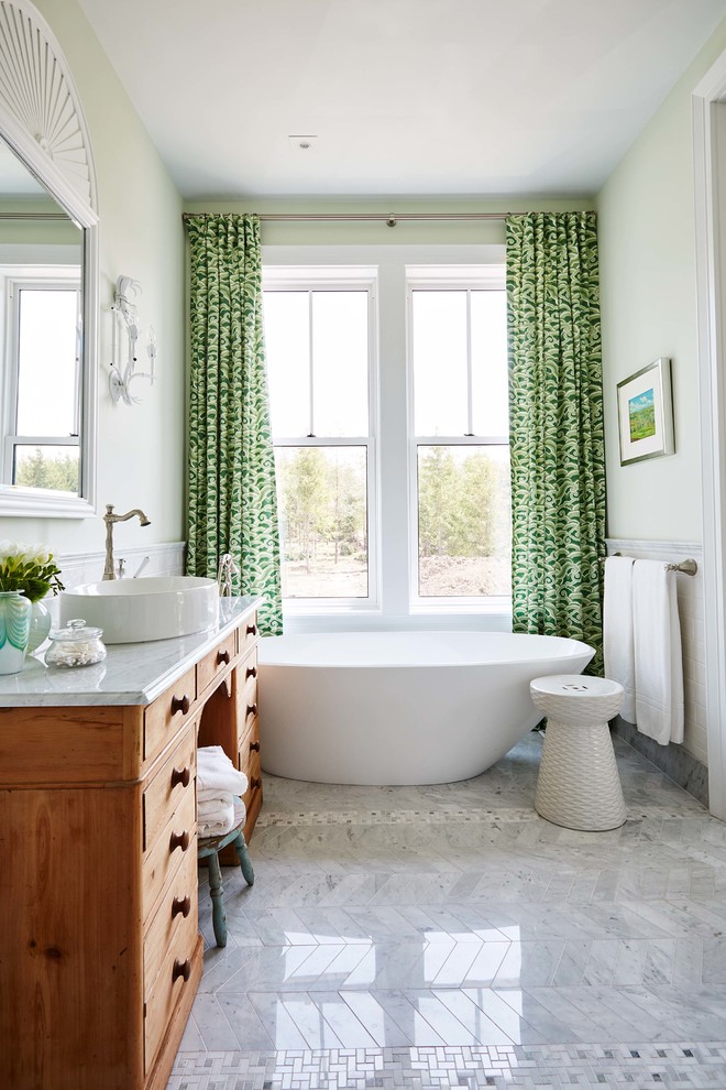 Aménagement d'une salle de bain campagne en bois clair avec un placard à porte plane, une baignoire indépendante, un mur vert et une vasque.