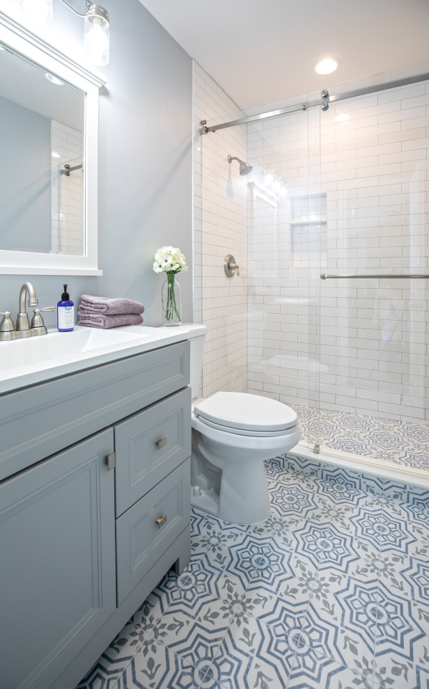 Inspiration för ett litet lantligt vit vitt badrum med dusch, med grå skåp, en dusch i en alkov, en toalettstol med separat cisternkåpa, vit kakel, keramikplattor, blå väggar, klinkergolv i porslin, ett integrerad handfat, bänkskiva i akrylsten, flerfärgat golv, dusch med skjutdörr och luckor med infälld panel