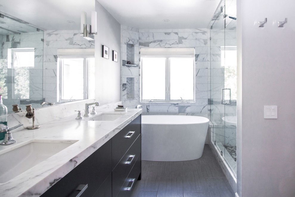 Modern inredning av ett mellanstort vit vitt en-suite badrum, med släta luckor, svarta skåp, ett fristående badkar, våtrum, en toalettstol med hel cisternkåpa, vit kakel, stenkakel, grå väggar, klinkergolv i porslin, ett undermonterad handfat och marmorbänkskiva