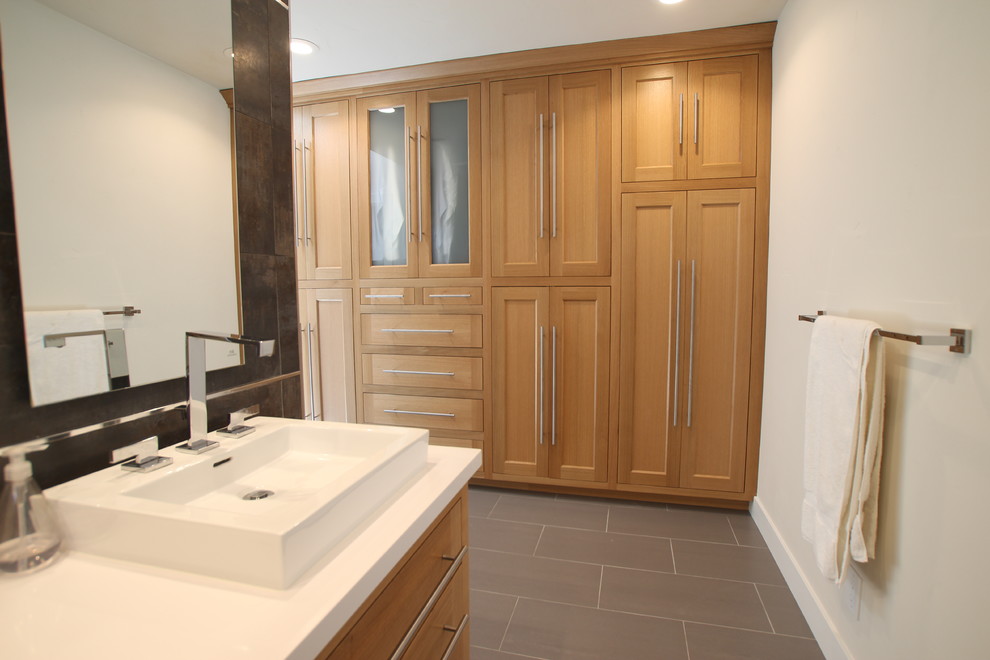 Modelo de cuarto de baño actual con lavabo sobreencimera, armarios con paneles lisos, puertas de armario de madera clara y encimera de granito