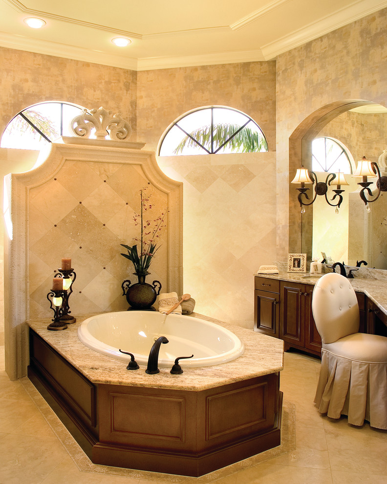 マイアミにある高級な広い地中海スタイルのおしゃれなマスターバスルーム (落し込みパネル扉のキャビネット、濃色木目調キャビネット、御影石の洗面台、ドロップイン型浴槽、オープン型シャワー、ベージュのタイル、石タイル、ベージュの壁) の写真
