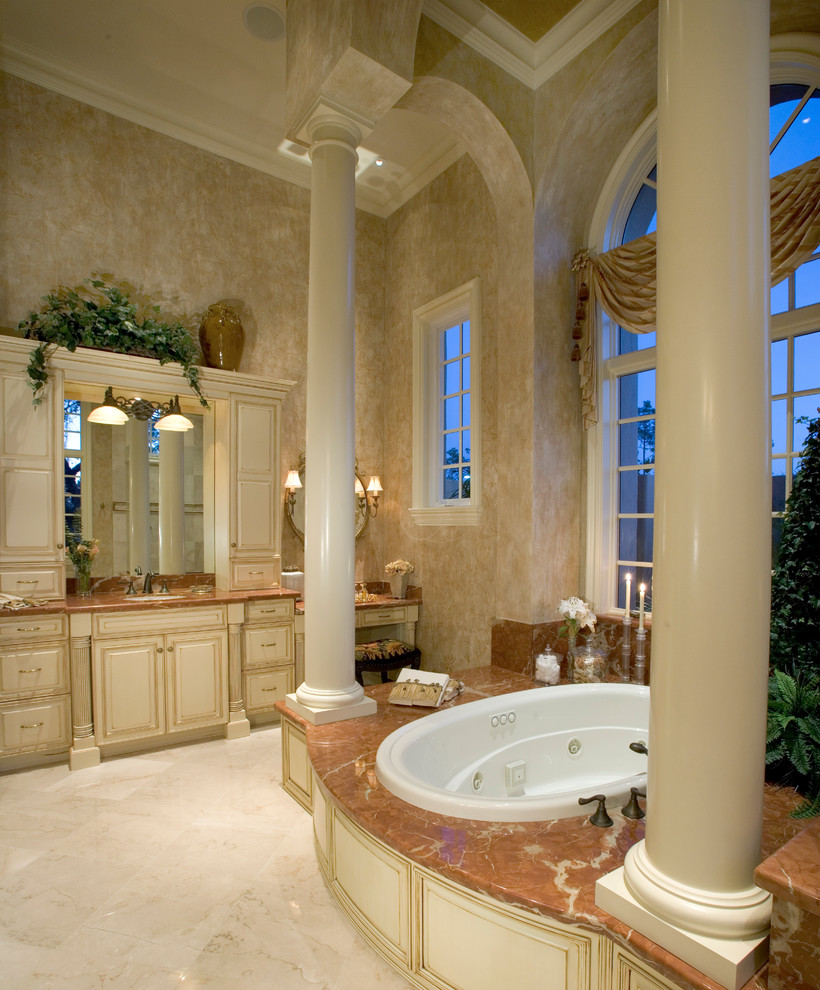 Mediterranean bathroom in Miami with raised-panel cabinets, beige cabinets, a built-in bath and beige floors.