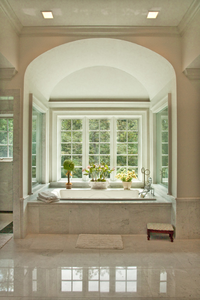 Inredning av ett lantligt badrum, med ett platsbyggt badkar, stenkakel och marmorgolv