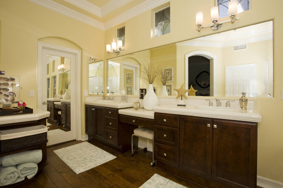 Klassisches Badezimmer mit Einbauwaschbecken, profilierten Schrankfronten, dunklen Holzschränken, gefliestem Waschtisch, weißen Fliesen, gelber Wandfarbe und weißer Waschtischplatte in San Diego