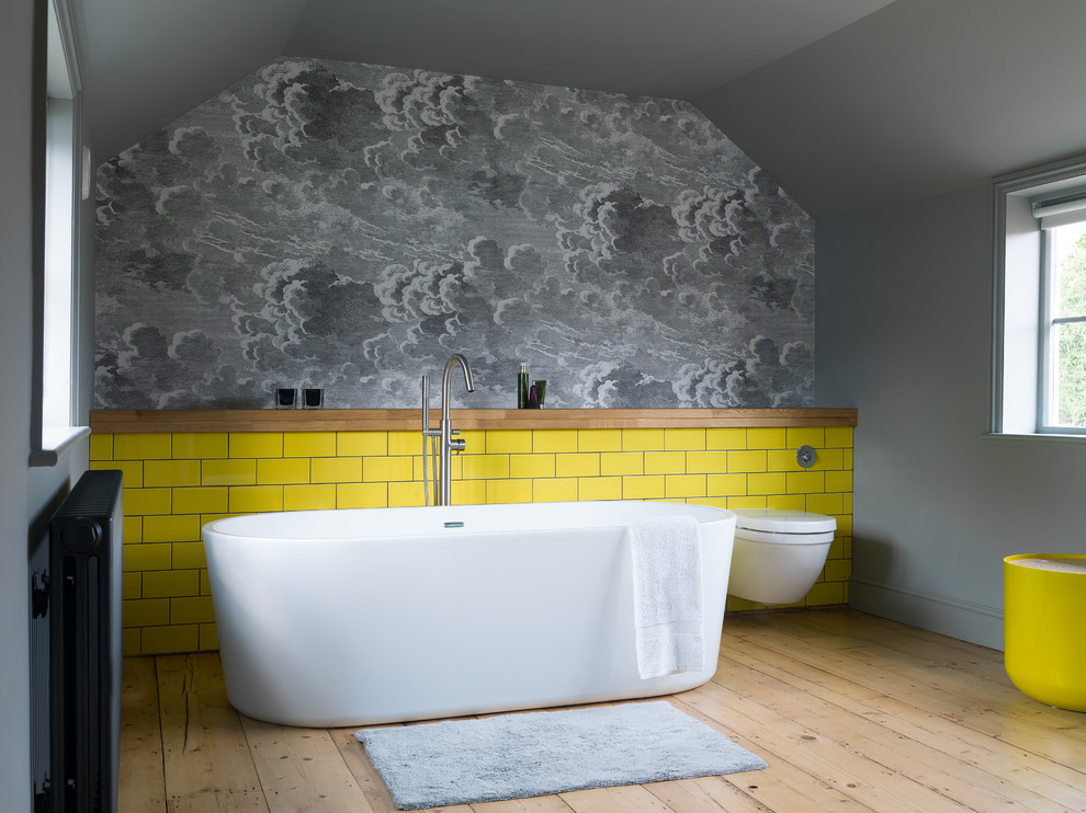 Idéer för ett lantligt badrum med dusch, med ett fristående badkar, en vägghängd toalettstol, gul kakel, grå väggar, beiget golv, keramikplattor och ljust trägolv