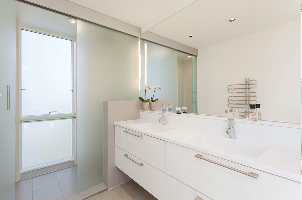 На фото: ванная комната в современном стиле с монолитной раковиной, плоскими фасадами, белыми фасадами, серой плиткой и белой столешницей с
