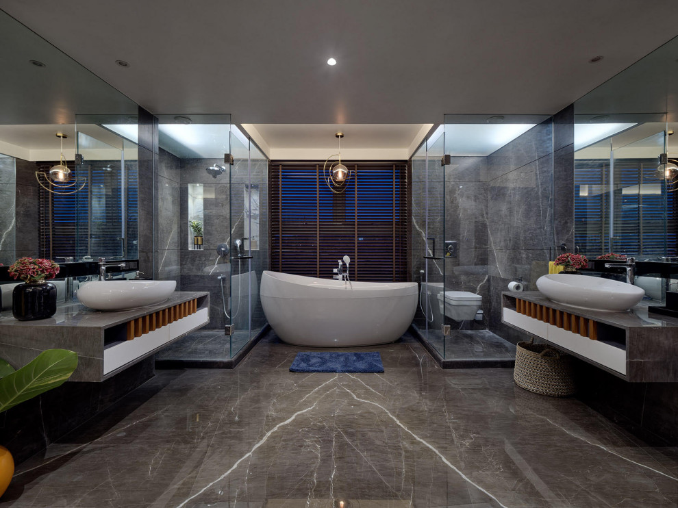 Modern inredning av ett mycket stort grå grått en-suite badrum, med släta luckor, vita skåp, ett fristående badkar, en hörndusch, en vägghängd toalettstol, grå kakel, ett fristående handfat, grått golv och dusch med gångjärnsdörr