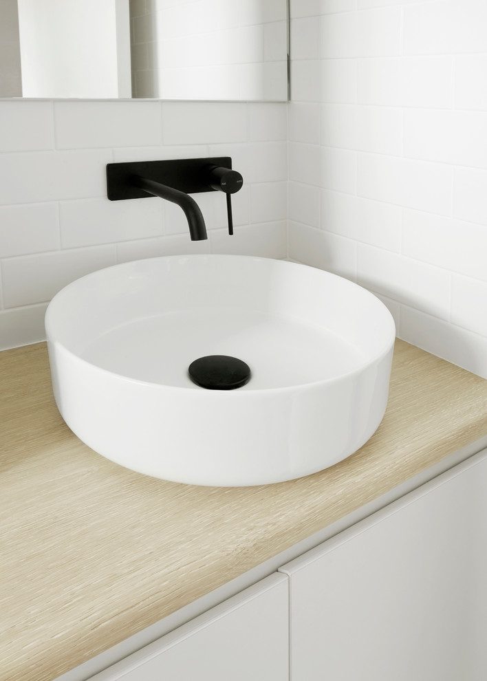 Minimalistisk inredning av ett litet badrum, med luckor med lamellpanel, vita skåp, en kantlös dusch, vit kakel, tunnelbanekakel, klinkergolv i keramik, laminatbänkskiva, grått golv och dusch med gångjärnsdörr