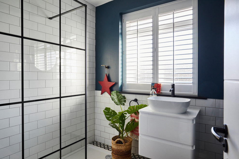 Modernes Badezimmer mit flächenbündigen Schrankfronten, weißen Schränken, weißen Fliesen, Metrofliesen, Aufsatzwaschbecken, buntem Boden und weißer Waschtischplatte in London