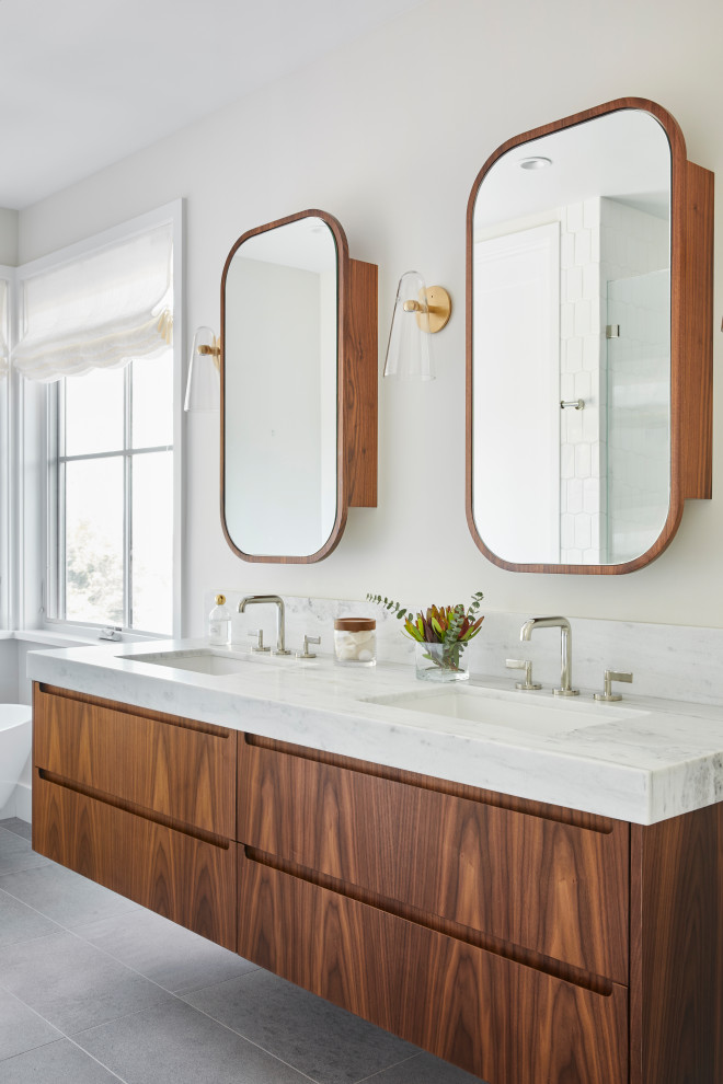 Inredning av ett minimalistiskt vit vitt badrum, med släta luckor, skåp i mellenmörkt trä, vita väggar, ett undermonterad handfat och grått golv
