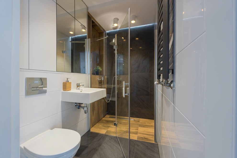 Exempel på ett skandinaviskt badrum med dusch, med en kantlös dusch, en vägghängd toalettstol, brun kakel, grå kakel, vit kakel, vita väggar, ett väggmonterat handfat, grått golv och dusch med gångjärnsdörr