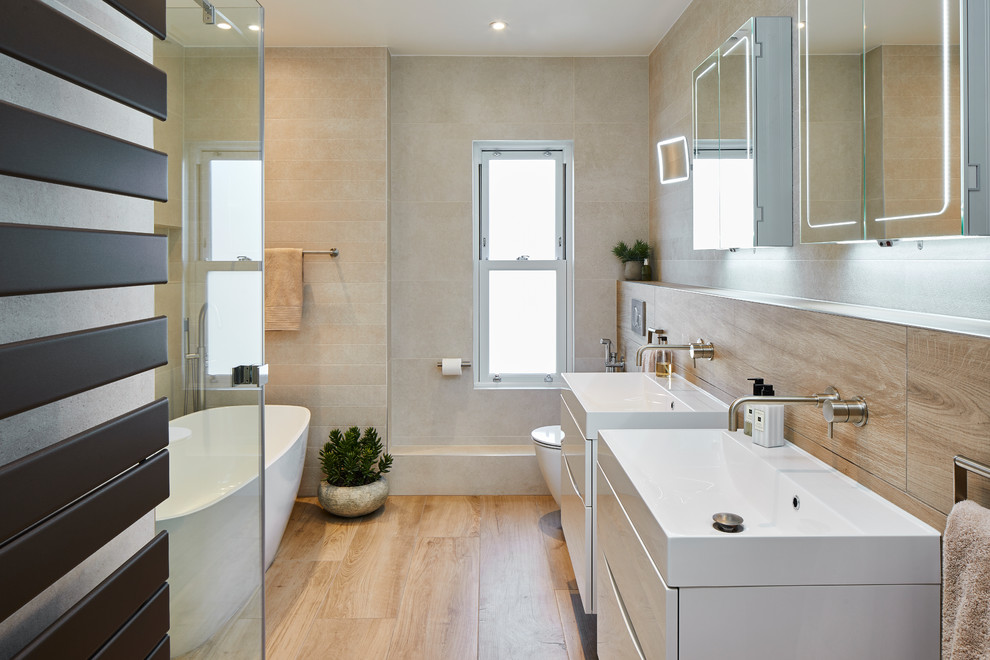 Design ideas for a scandi ensuite wet room bathroom in Surrey with white cabinets, a freestanding bath, a one-piece toilet, beige tiles, ceramic tiles, beige walls, ceramic flooring, a wall-mounted sink, solid surface worktops, brown floors, a hinged door and white worktops.