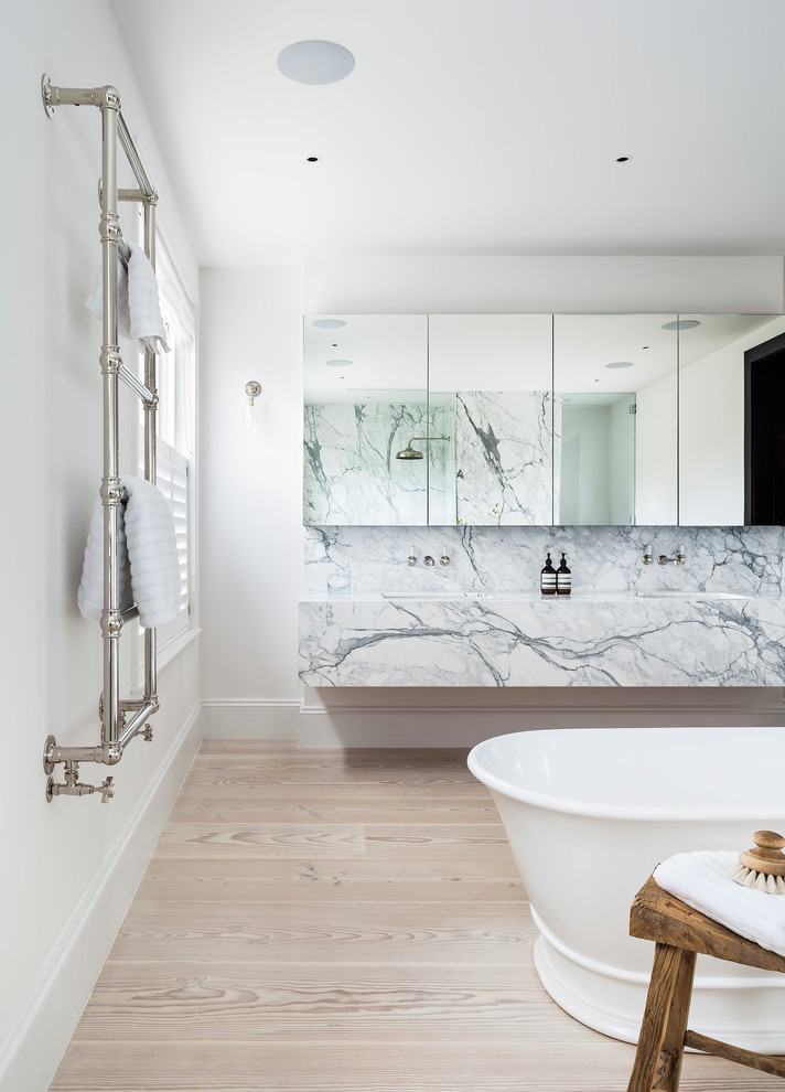 ロンドンにある北欧スタイルのおしゃれな浴室 (置き型浴槽、白いタイル、白い壁、淡色無垢フローリング、フラットパネル扉のキャビネット、壁付け型シンク、大理石の洗面台、大理石タイル) の写真