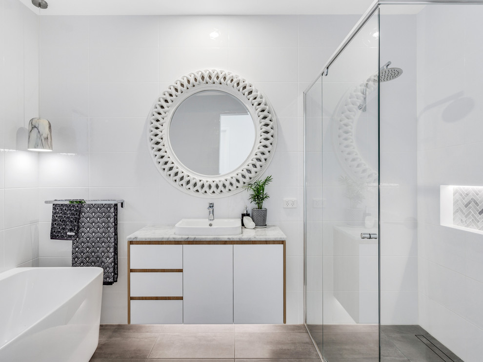 На фото: большая ванная комната в современном стиле с белой плиткой, керамической плиткой, полом из керамической плитки, настольной раковиной, мраморной столешницей, черным полом и отдельно стоящей ванной