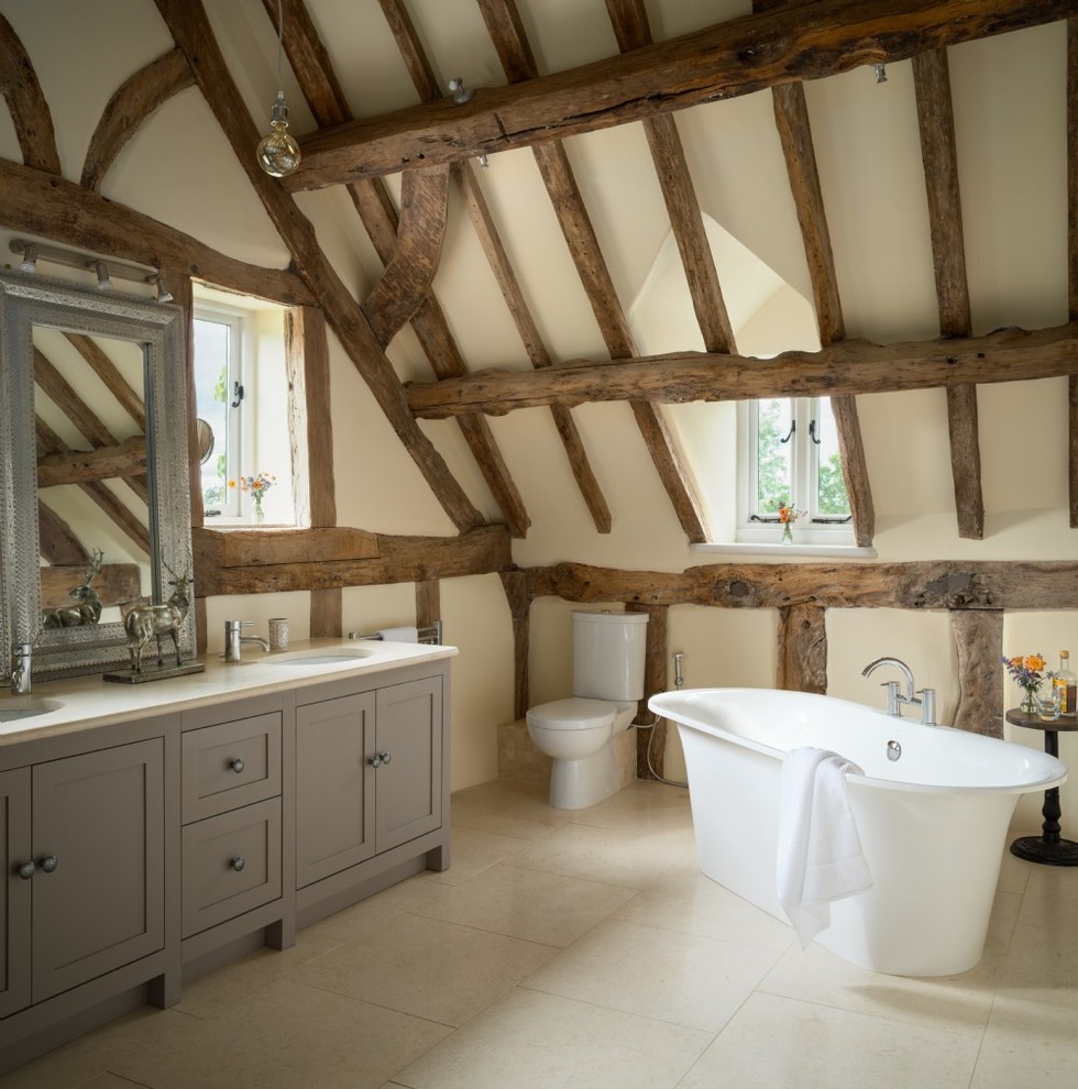 Inspiration for a medium sized rustic bathroom in Cheshire with recessed-panel cabinets, grey cabinets, a freestanding bath, a two-piece toilet, beige walls, a submerged sink, white floors and white worktops.