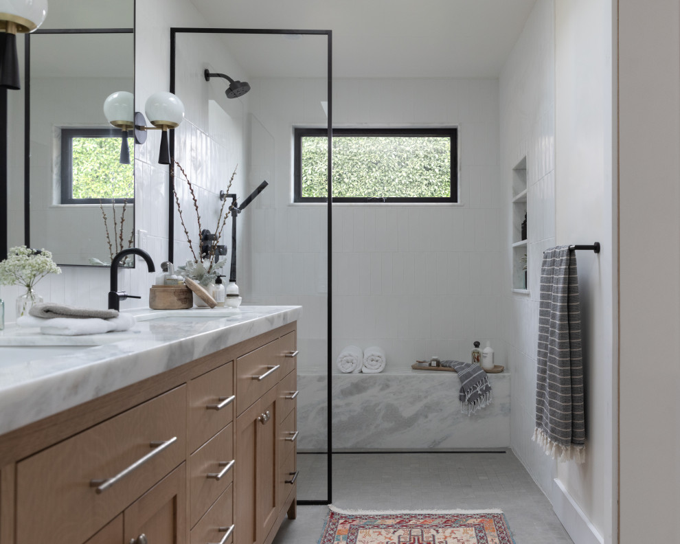 Inredning av ett klassiskt stort vit vitt badrum med dusch, med luckor med infälld panel, skåp i ljust trä, en kantlös dusch, en bidé, vit kakel, porslinskakel, vita väggar, kalkstensgolv, ett undermonterad handfat, marmorbänkskiva, grått golv och dusch med gångjärnsdörr