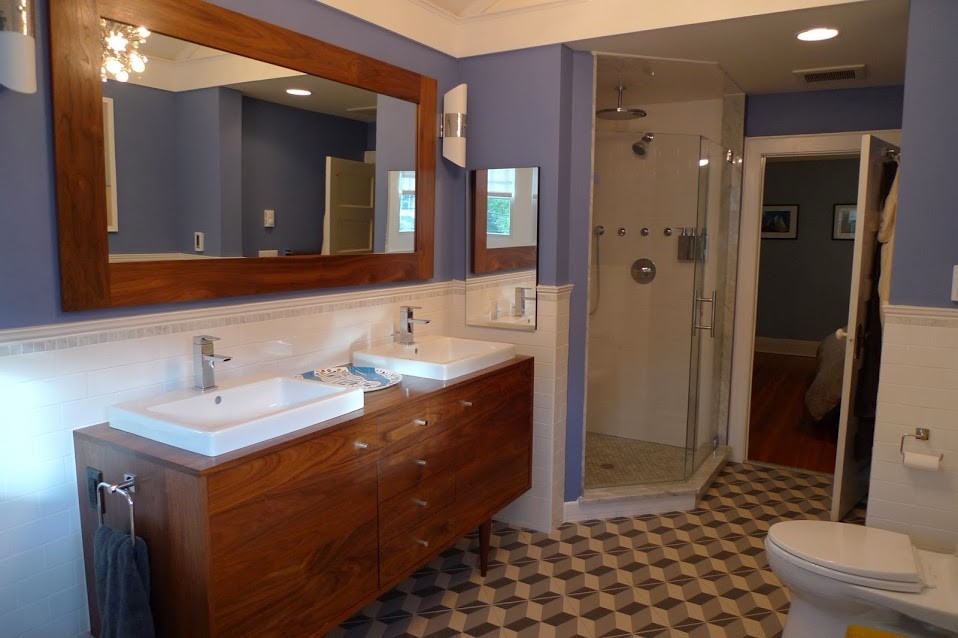 Inredning av ett 60 tals stort en-suite badrum, med släta luckor, skåp i mellenmörkt trä, ett fristående badkar, en hörndusch, en toalettstol med hel cisternkåpa, vit kakel, tunnelbanekakel, blå väggar, cementgolv, ett fristående handfat, träbänkskiva, flerfärgat golv och dusch med gångjärnsdörr