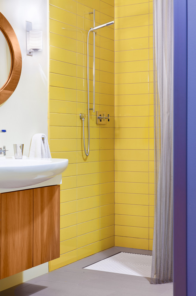 Foto på ett funkis badrum, med ett väggmonterat handfat, släta luckor, skåp i mellenmörkt trä, en kantlös dusch och gul kakel