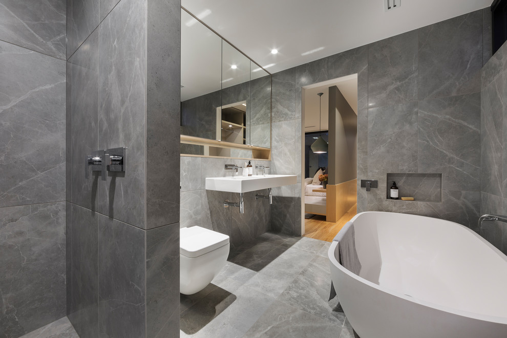 Cette photo montre une salle de bain principale tendance avec une baignoire indépendante, une douche ouverte, WC suspendus, un mur gris, un sol en marbre, un lavabo suspendu, un sol gris et aucune cabine.