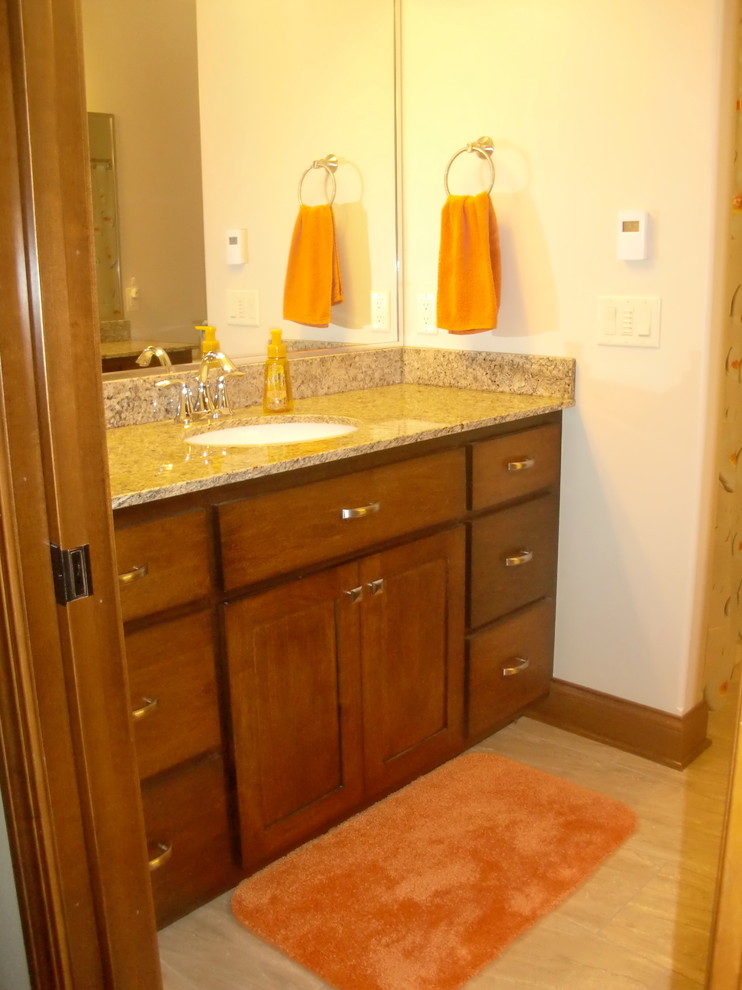 Cette photo montre une salle de bain chic en bois brun de taille moyenne pour enfant avec un lavabo encastré, un placard à porte shaker, un plan de toilette en granite, un carrelage beige, des carreaux de porcelaine, un mur gris et un sol en carrelage de porcelaine.