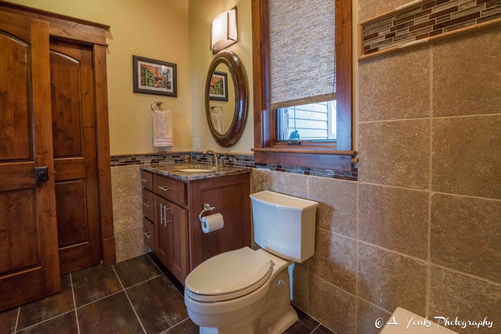 Example of a mid-sized mountain style 3/4 beige tile, brown tile, gray tile and ceramic tile slate floor bathroom design in Other with shaker cabinets, medium tone wood cabinets, a one-piece toilet, yellow walls, an undermount sink and granite countertops