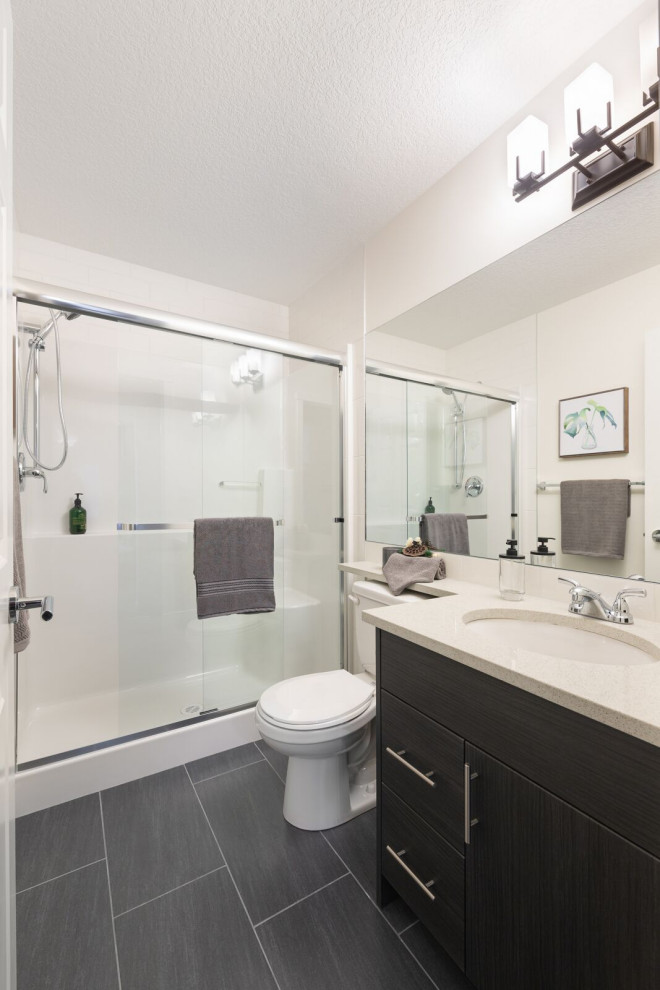 Photo of a small contemporary shower room bathroom in Calgary with flat-panel cabinets, black cabinets, an alcove shower, a two-piece toilet, white tiles, white walls, a submerged sink, black floors, a sliding door and white worktops.