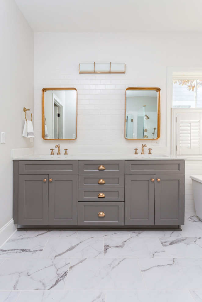 Inspiration for a large coastal master white tile and subway tile marble floor and white floor freestanding bathtub remodel in Charleston with recessed-panel cabinets, gray cabinets, a two-piece toilet, gray walls, an integrated sink, quartz countertops, a hinged shower door and white countertops