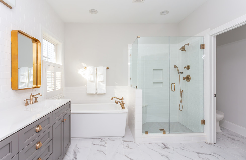 На фото: большая главная ванная комната в морском стиле с фасадами с утопленной филенкой, серыми фасадами, отдельно стоящей ванной, раздельным унитазом, белой плиткой, плиткой кабанчик, серыми стенами, мраморным полом, монолитной раковиной, столешницей из искусственного кварца, белым полом, душем с распашными дверями и белой столешницей