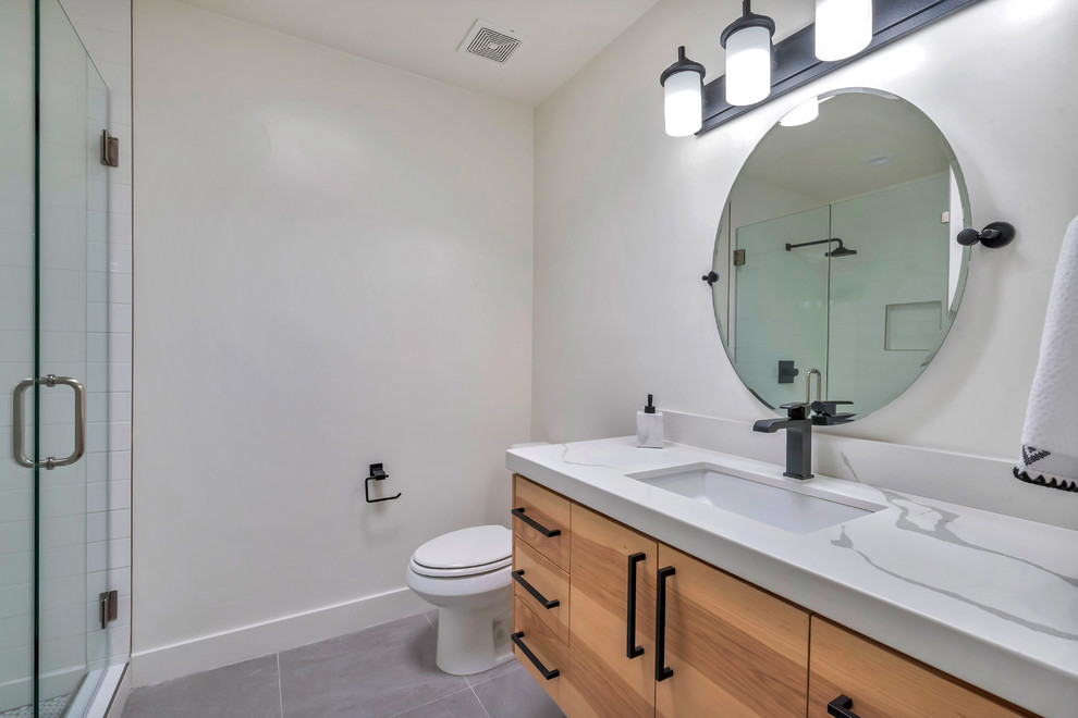 Mid-sized trendy master gray floor, single-sink and ceramic tile corner shower photo in Phoenix with flat-panel cabinets, light wood cabinets, a one-piece toilet, white walls, an undermount sink, a hinged shower door, quartz countertops, white countertops, a niche and a floating vanity