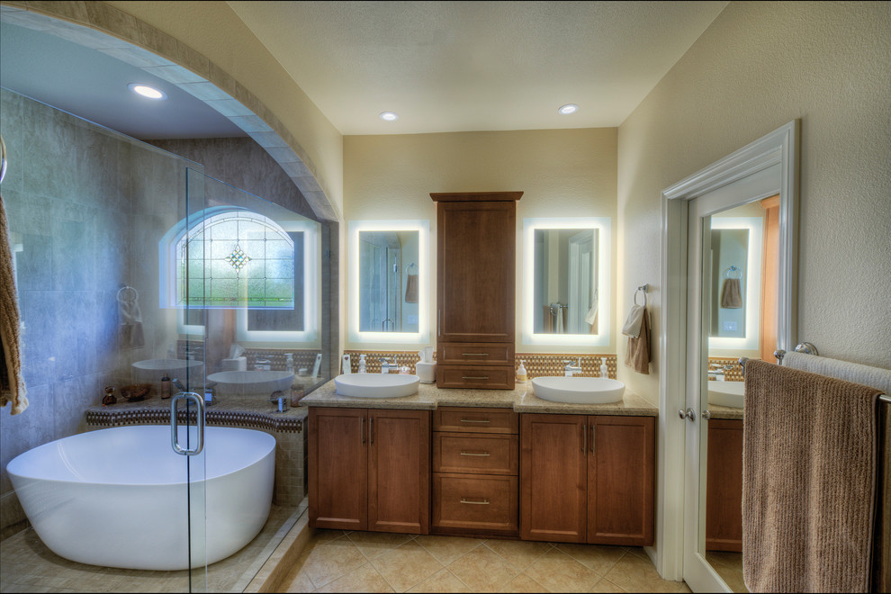 This is an example of an expansive contemporary ensuite bathroom in San Diego with raised-panel cabinets, brown cabinets, a japanese bath, a shower/bath combination, a two-piece toilet, beige tiles, travertine tiles, beige walls, travertine flooring, a vessel sink, granite worktops, beige floors, a hinged door and brown worktops.