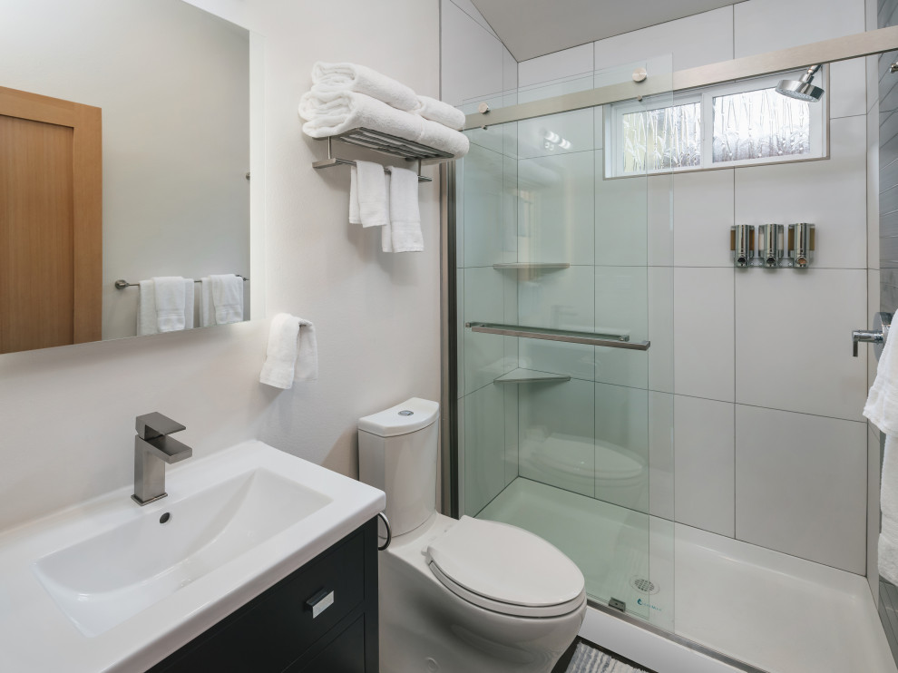 Inspiration for a medium sized modern ensuite bathroom in Portland with freestanding cabinets, black cabinets, a two-piece toilet, white tiles, porcelain tiles, white walls, concrete flooring, an integrated sink, solid surface worktops, multi-coloured floors, a sliding door and white worktops.