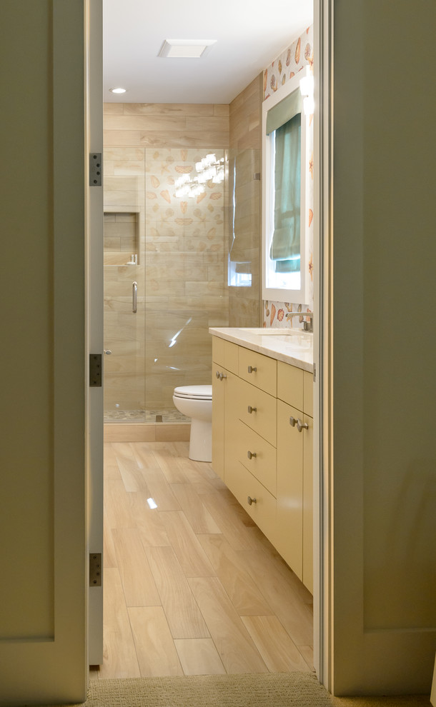 Inspiration for a mid-sized coastal 3/4 beige tile and porcelain tile porcelain tile and beige floor alcove shower remodel in Charleston with flat-panel cabinets, a one-piece toilet, an undermount sink, quartzite countertops, a hinged shower door and yellow cabinets